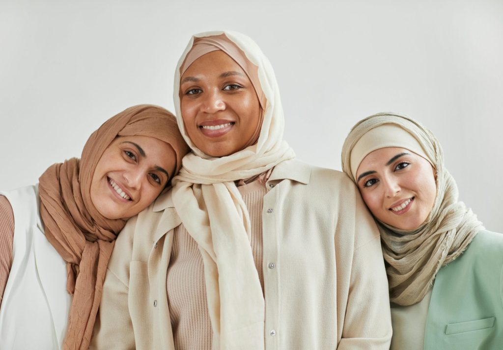 Three smiling women in hijabs, representing diversity and friendship in a studio setting.